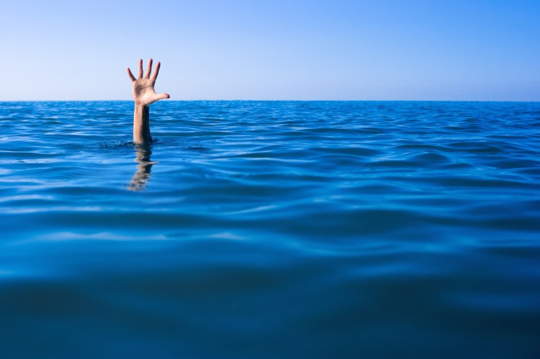 Help needed. Drowning man's hand in sea or ocean.